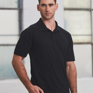 A man in a black polo shirt stands against an industrial background, featuring short sleeves and a standard collar.