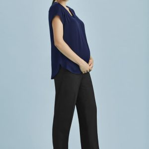 A woman wearing a navy top and black maternity pants stands against a light blue background, smiling and holding her belly.