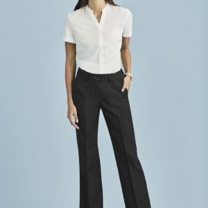 A woman in a white shirt and black relaxed pants poses against a light blue background, showcasing a polished outfit.