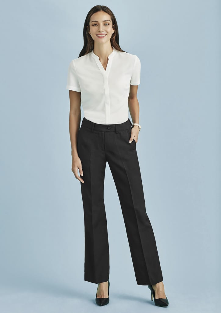 A woman in a white shirt and black relaxed pants poses against a light blue background, showcasing a polished outfit.
