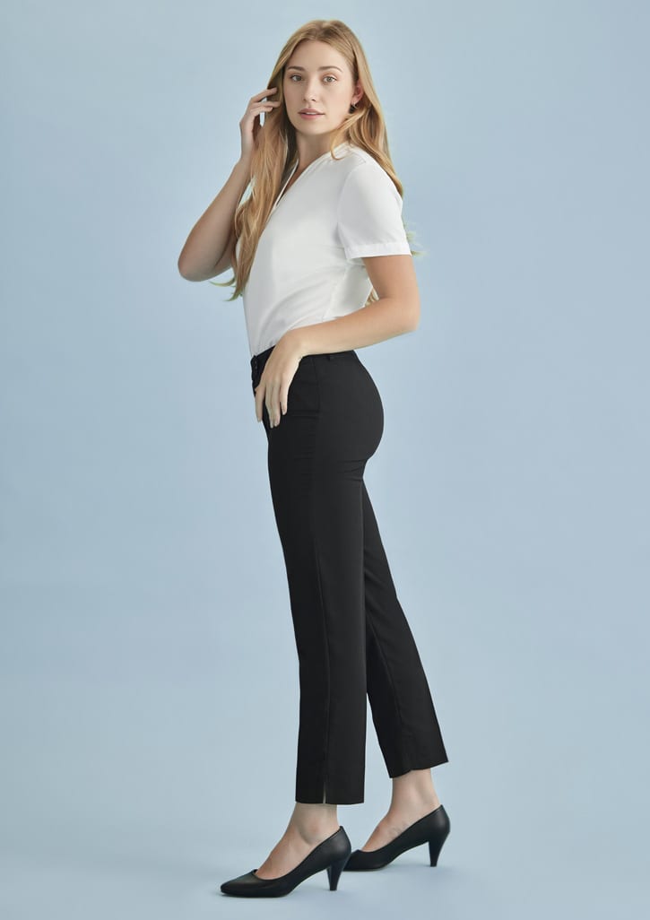 A woman poses in black slim leg pants with a fitted white top against a light blue background.