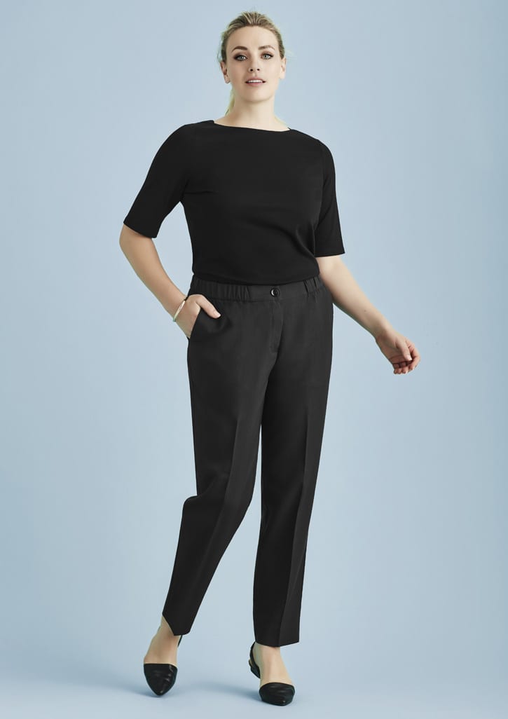 A woman in a black top and black ultra comfort waist pants poses against a light blue background. The pants feature a waistband and pockets.