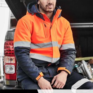 A man in a high-visibility orange jacket sits near a vehicle, wearing a beanie and dark pants. The image includes a logo.