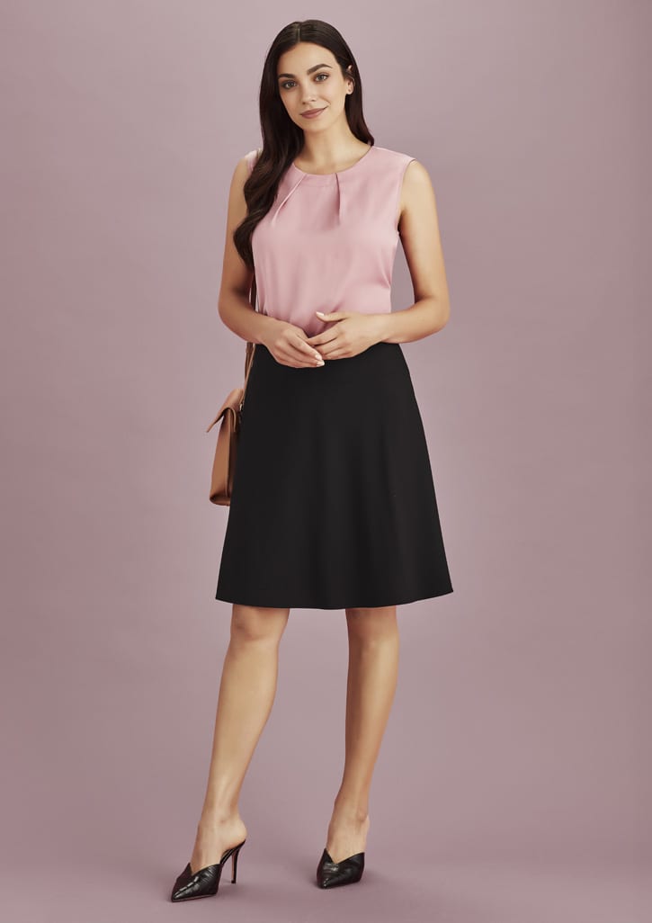 A woman stands wearing a pink top and a black flared skirt, accessorised with a handbag and high heels.