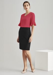 A model wears a pink top and a black multi-pleat skirt, standing against a neutral background. The skirt has a sleek design and waistband.