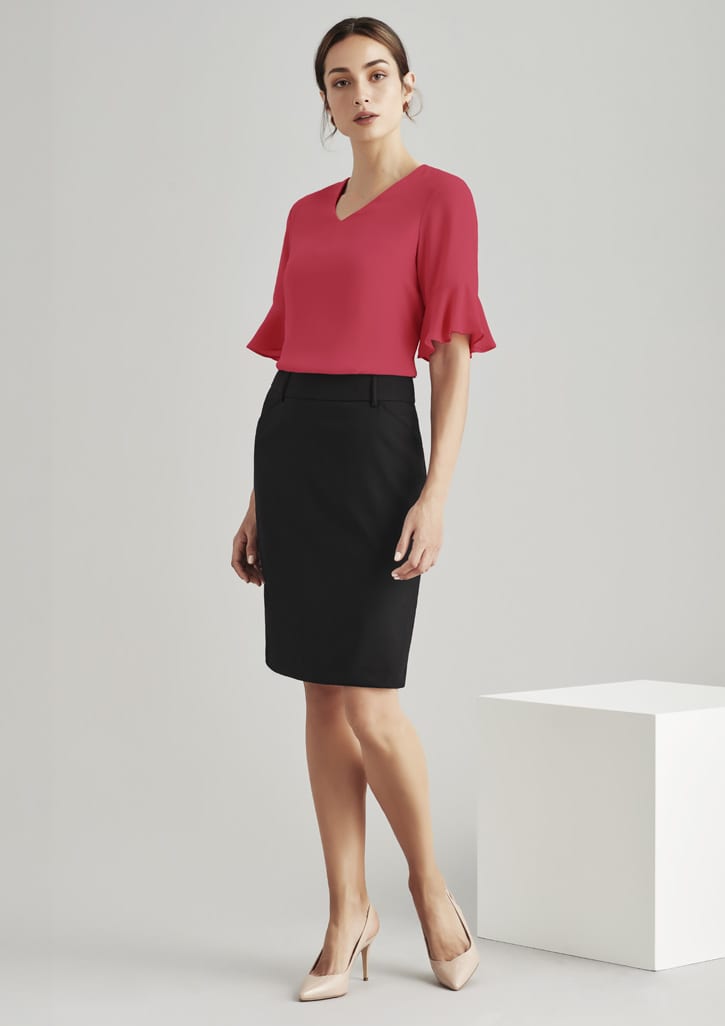 A model wears a pink top and a black multi-pleat skirt, standing against a neutral background. The skirt has a sleek design and waistband.