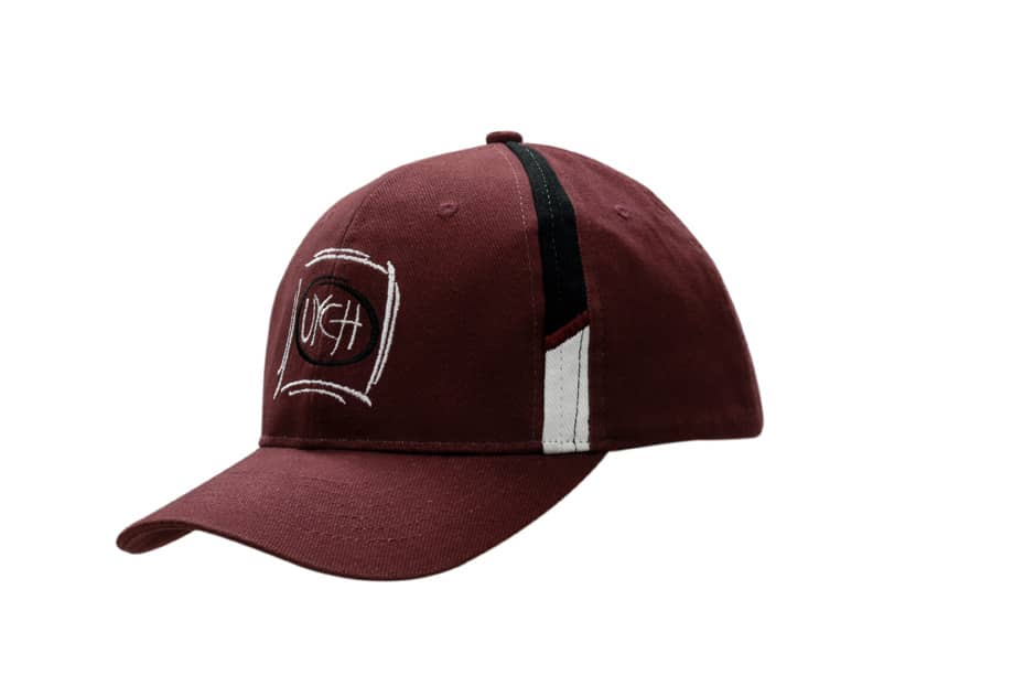 A burgundy cap with fabric inserts on the crown and a logo on the front. Features a curved brim and contrasting accents.