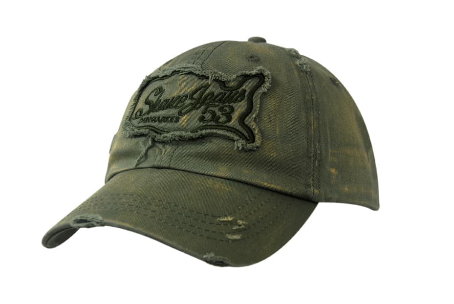 A green chino twill cap with distress marks on the crown and peak, featuring a logo on the front.