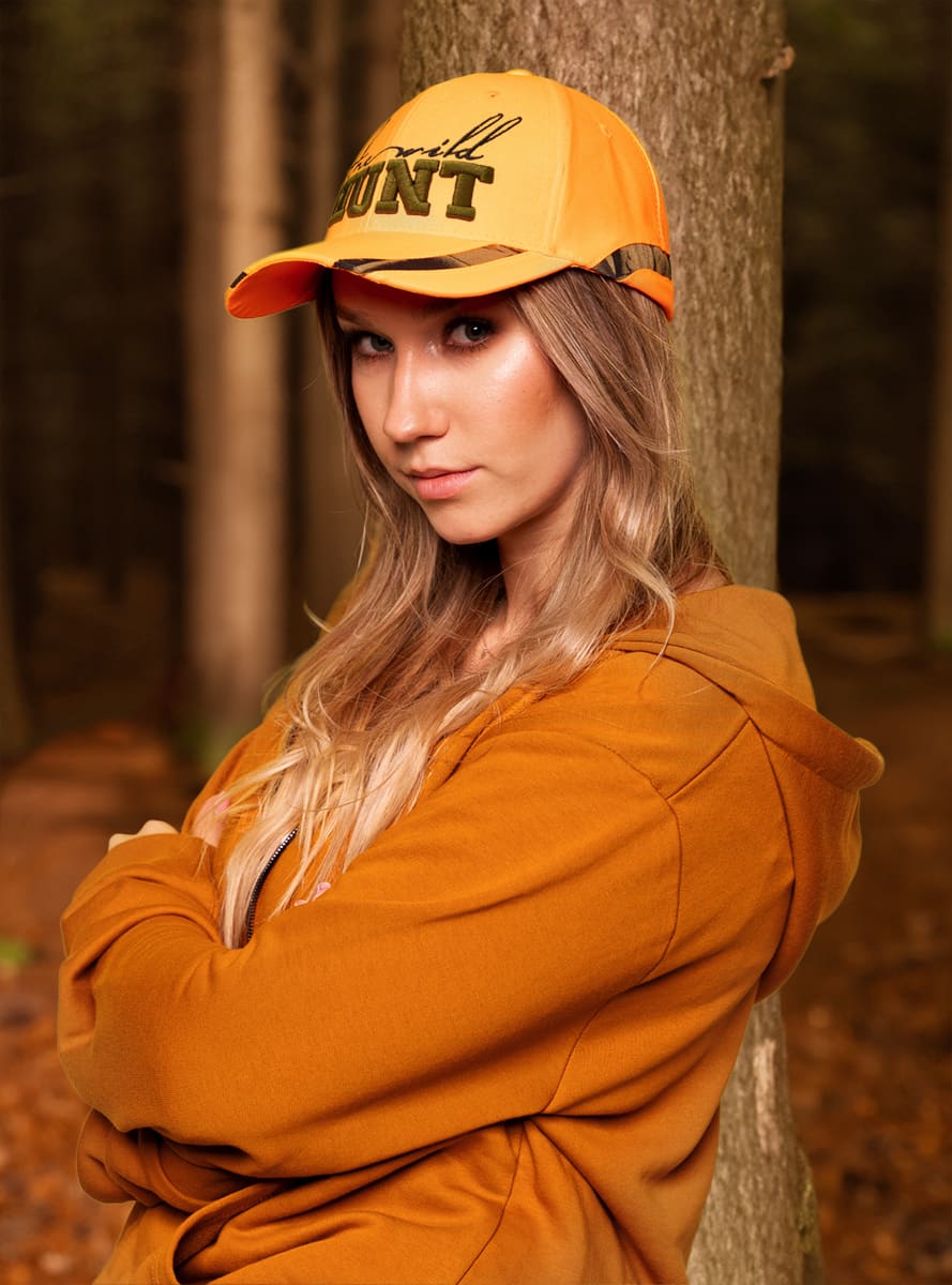 A cap featuring a bright orange visor and camo print inserts, worn by a woman in a forest setting.