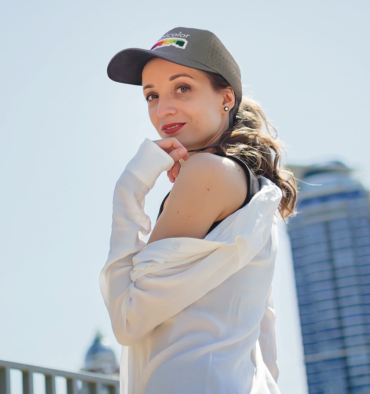 A woman poses outdoors wearing a grey breathable poly twill cap with circle perforations.