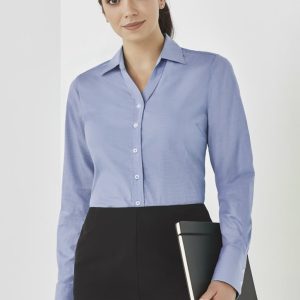 A woman in a light blue button-up long sleeve shirt holds a tablet, set against a neutral background.