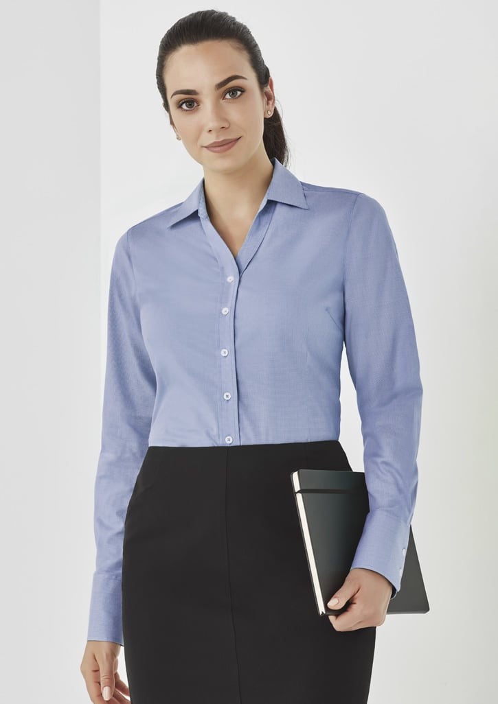 A woman in a light blue button-up long sleeve shirt holds a tablet, set against a neutral background.