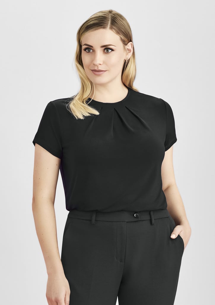 A woman wearing a black short sleeve top with a pleated design, paired with black trousers. The top features a logo.
