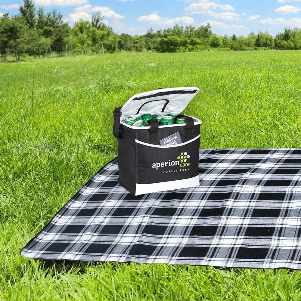 A black cooler bag sits on a checkered picnic blanket in a grassy field, with drinks visible inside.