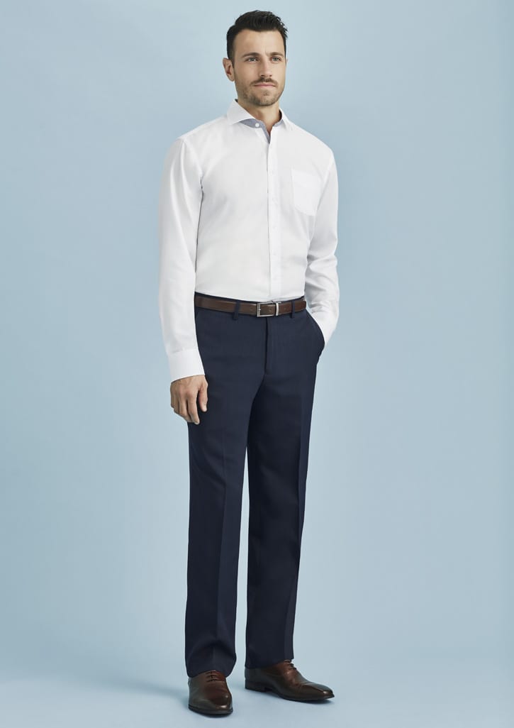 A man stands wearing flat front navy blue slacks paired with a white shirt and brown belt, against a light blue background.
