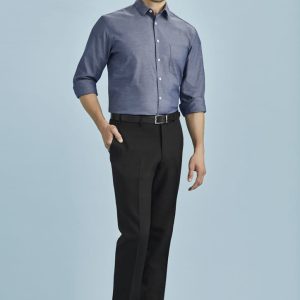A man wearing a blue shirt and black slimline pants, standing against a light blue background, with a logo visible.