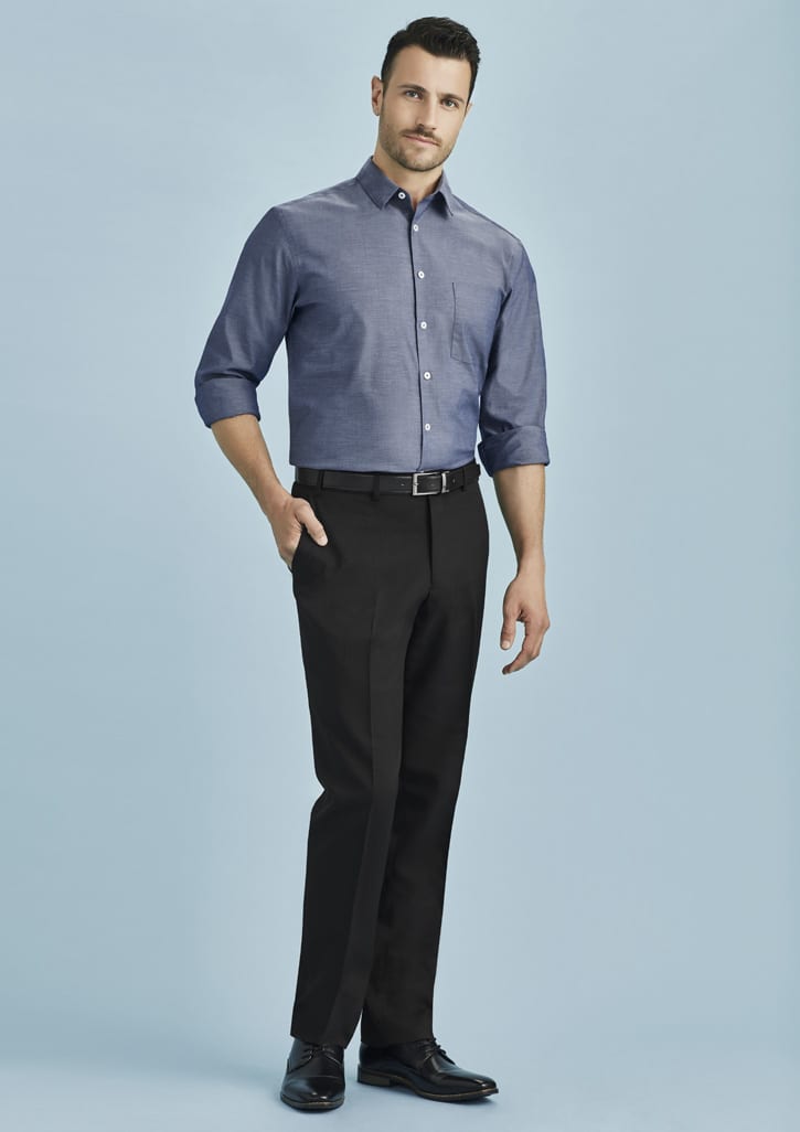 A man wearing a blue shirt and black slimline pants, standing against a light blue background, with a logo visible.