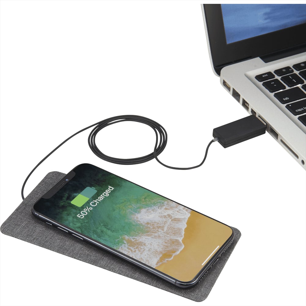 A grey wireless charging pad with a smartphone charging, connected via a cable to a laptop.