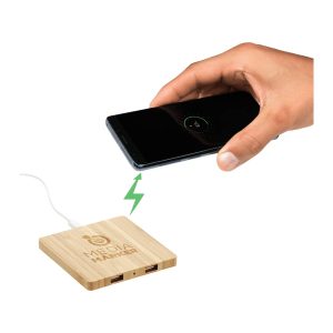 A bamboo wireless charging pad with dual outputs and a hand placing a smartphone on it.