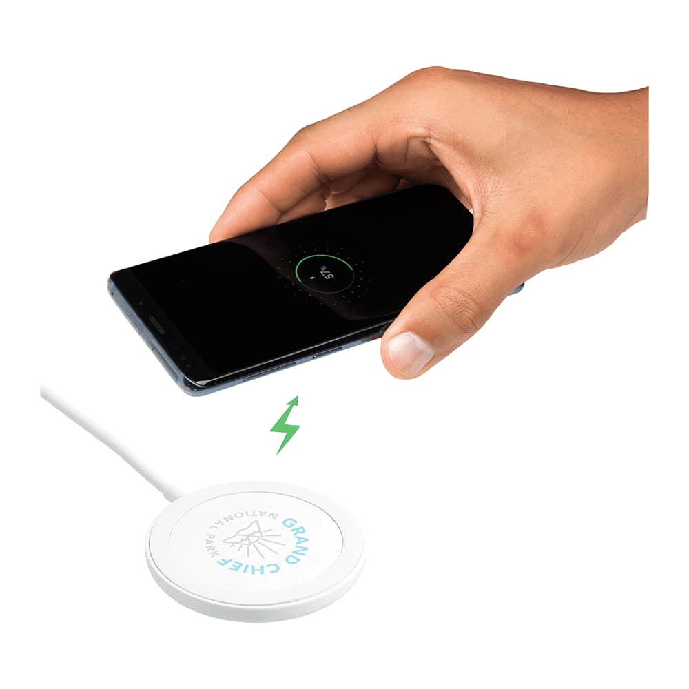 A wireless charging pad in white with a hand holding a smartphone above it, depicting the charging process.