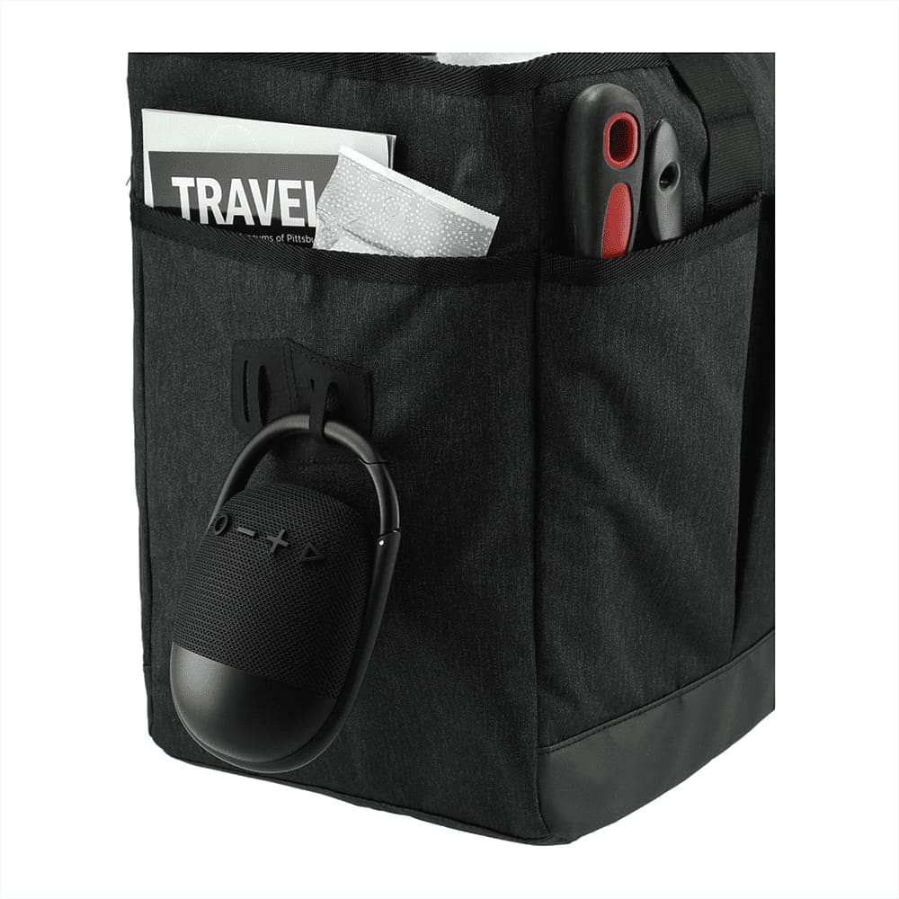 A black waterproof Bluetooth speaker hanging from a black bag pocket, alongside travel documents and a tool.