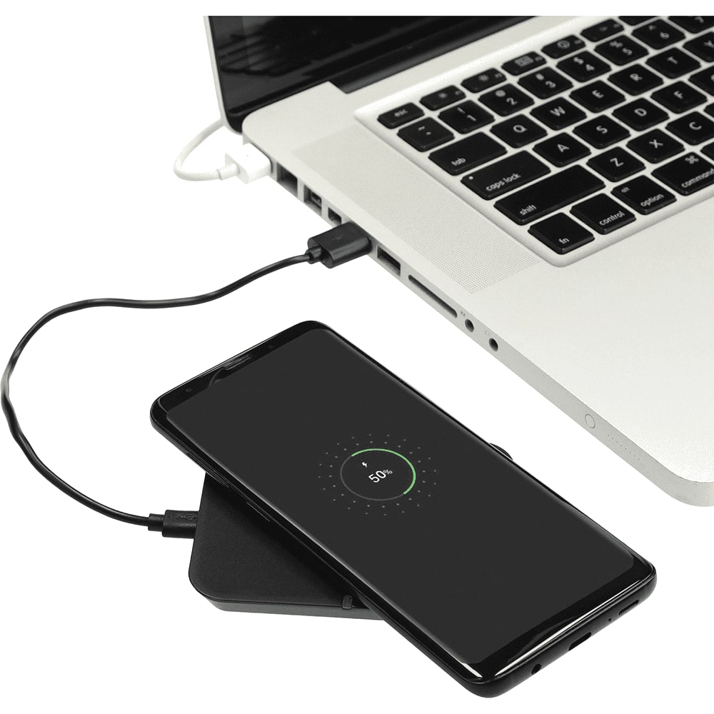 A wireless charging phone stand in black, with a smartphone on it, connected to a laptop by a charging cable.