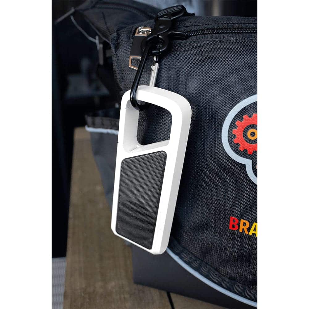 A white Bluetooth speaker with a mesh front and attachment clip, hanging from a bag. It features a logo on the bag.