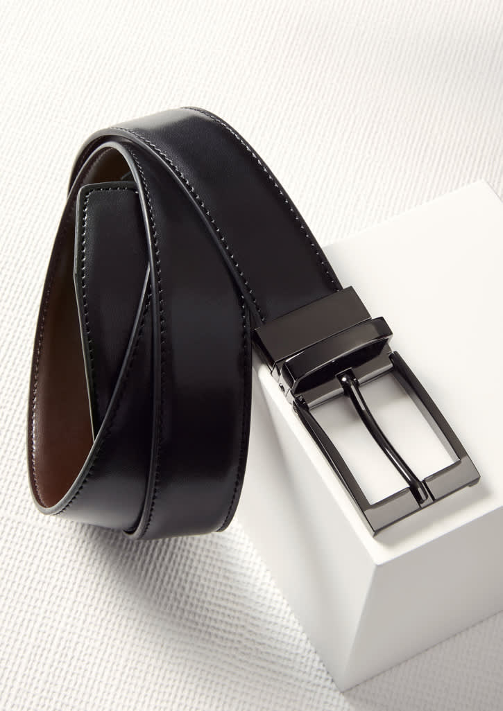 A men's leather reversible belt featuring black on one side and brown on the other, with a metallic buckle and branding.