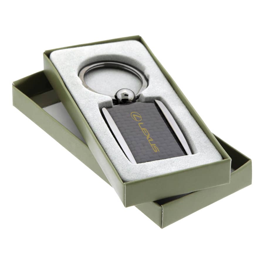 A carbon fibre keychain in a gift box with a metallic keyring and a logo. The box is green and the keychain is dark.