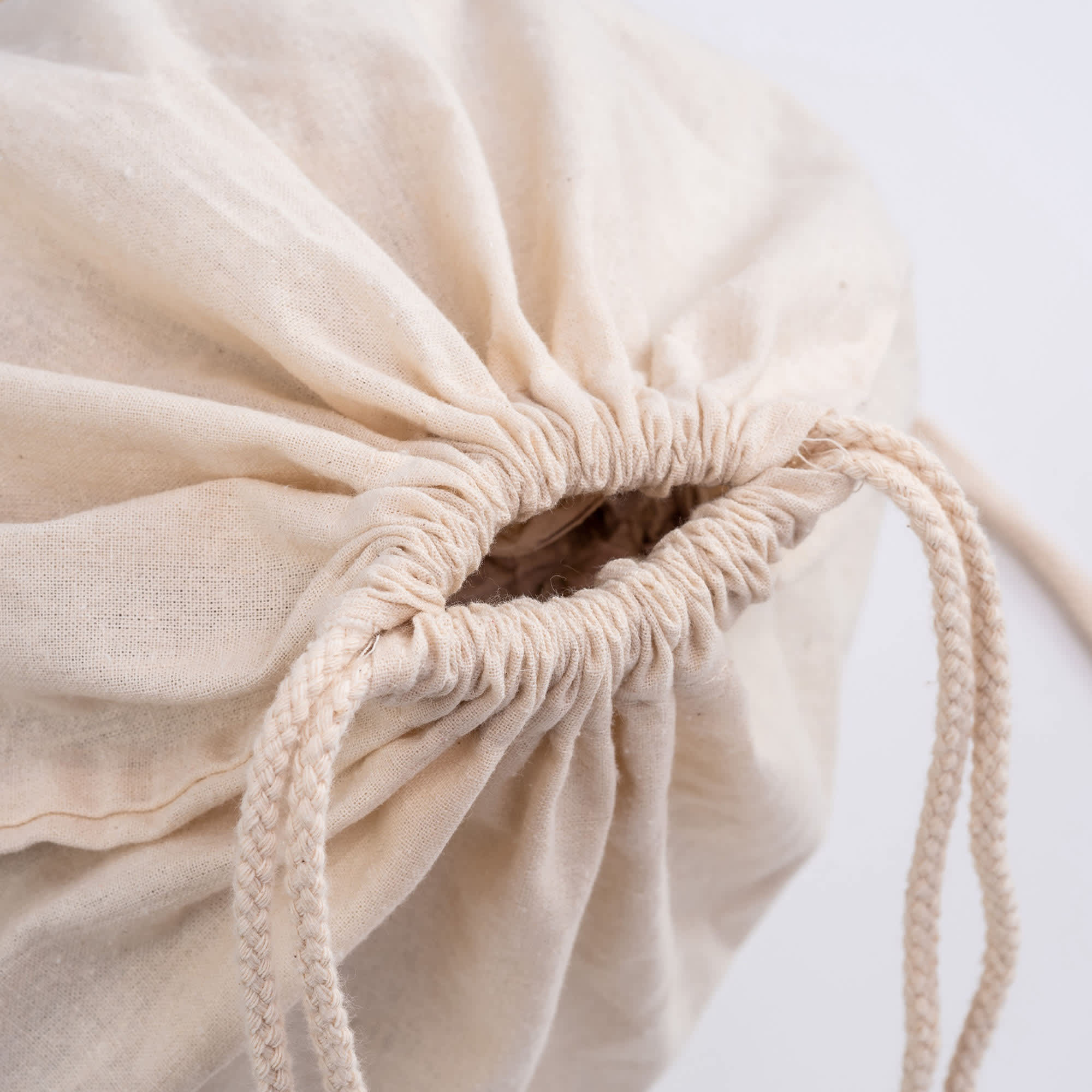 A beige drawstring bag with gathered fabric and twin corded drawstrings at the opening. It has a simple design.