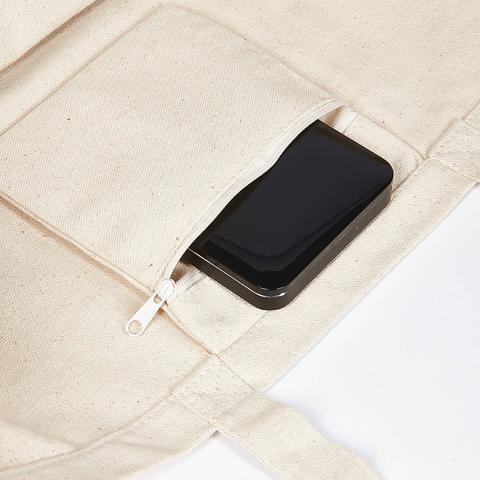 A beige canvas tote bag with a zipped pocket containing a black item. The bag has shoulder straps and stitching details.
