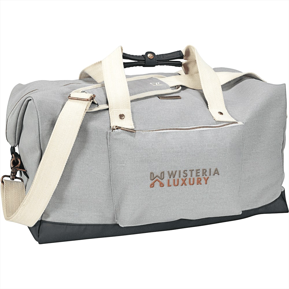 A grey cotton duffel bag with a black bottom, featuring fabric handles and a shoulder strap, along with a front zip pocket.