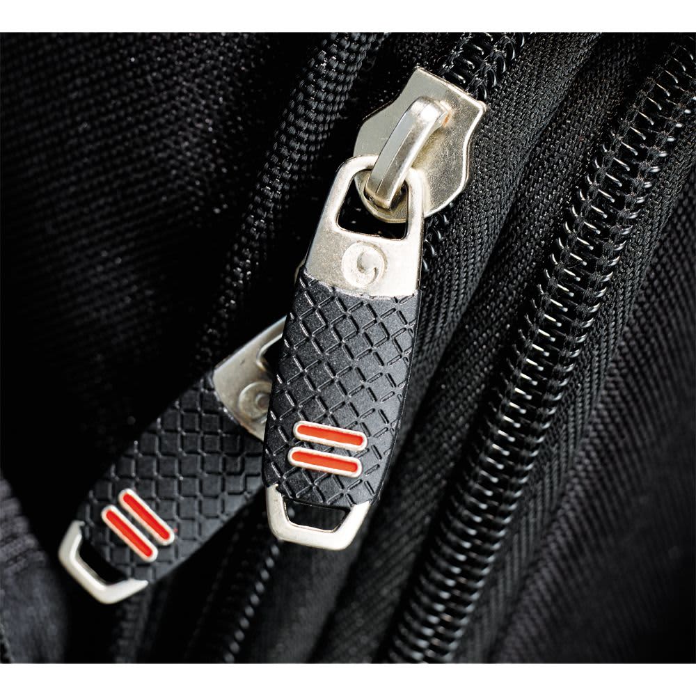 A grey backpack with a textured fabric and a logo patch. It features a zippered pocket and padded straps.