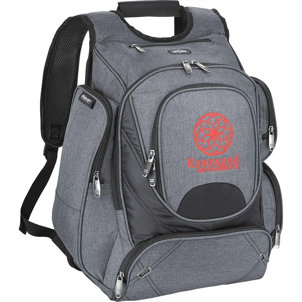 A black checkpoint-friendly backpack with multiple compartments sits beside a woman using a tablet.