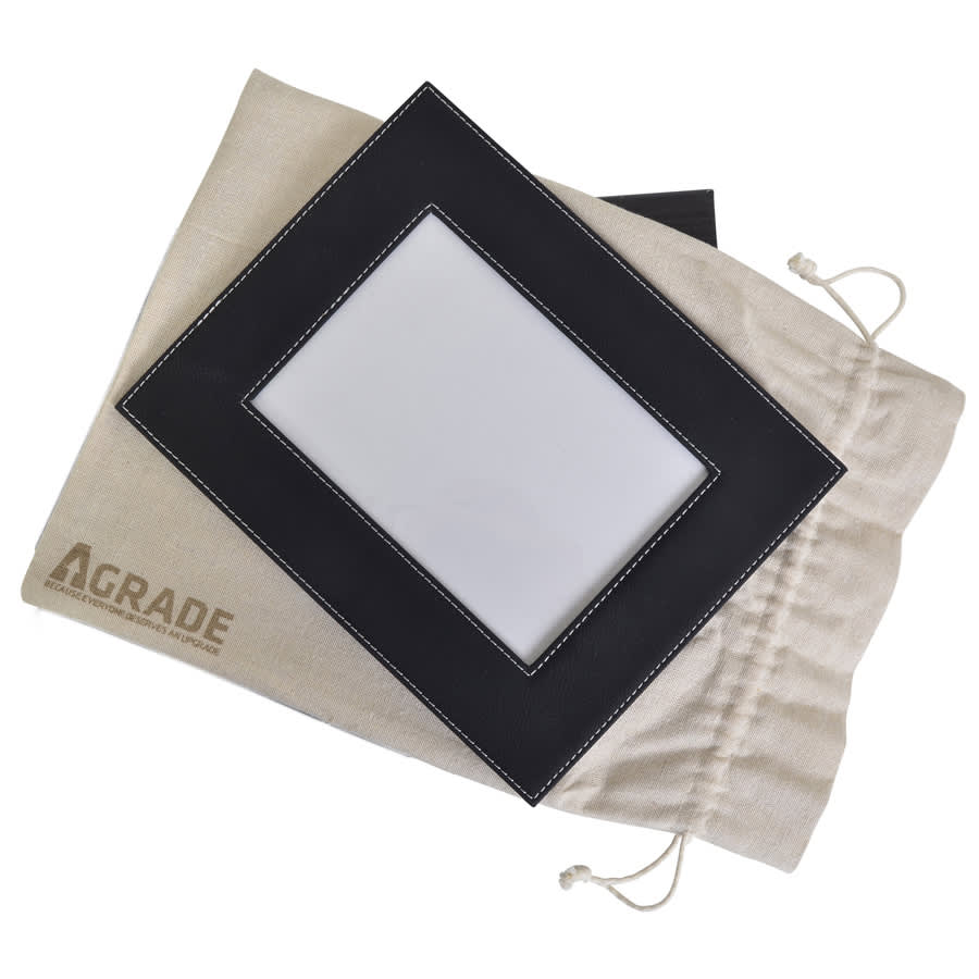 A black 5x7 photo frame with white stitching rests on a beige drawstring bag featuring a logo.