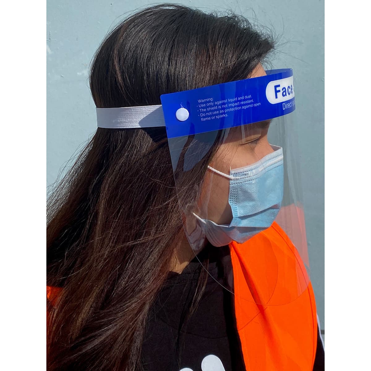 A full-length clear face shield with a blue headband, worn by a person in a bright orange vest and a surgical mask.