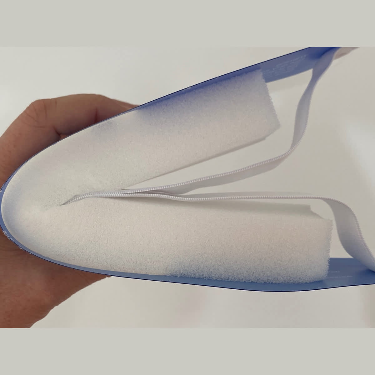 A blue full-length face shield held in a hand, featuring a white foam lining and elastic straps.