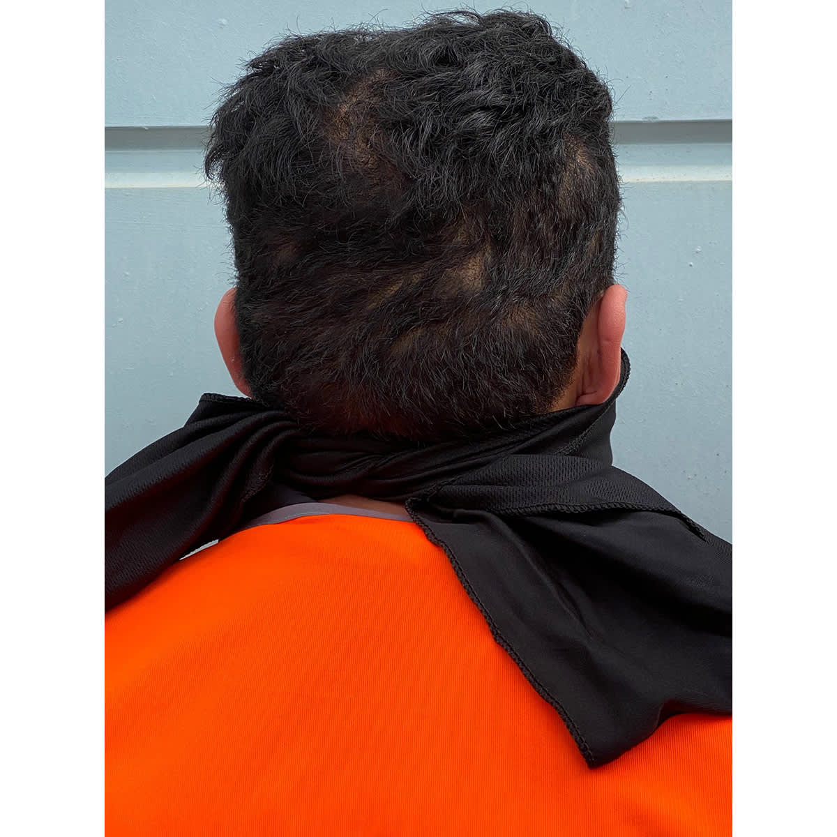 A person wearing an orange shirt with a black cooling towel tied around their neck, viewed from the back.