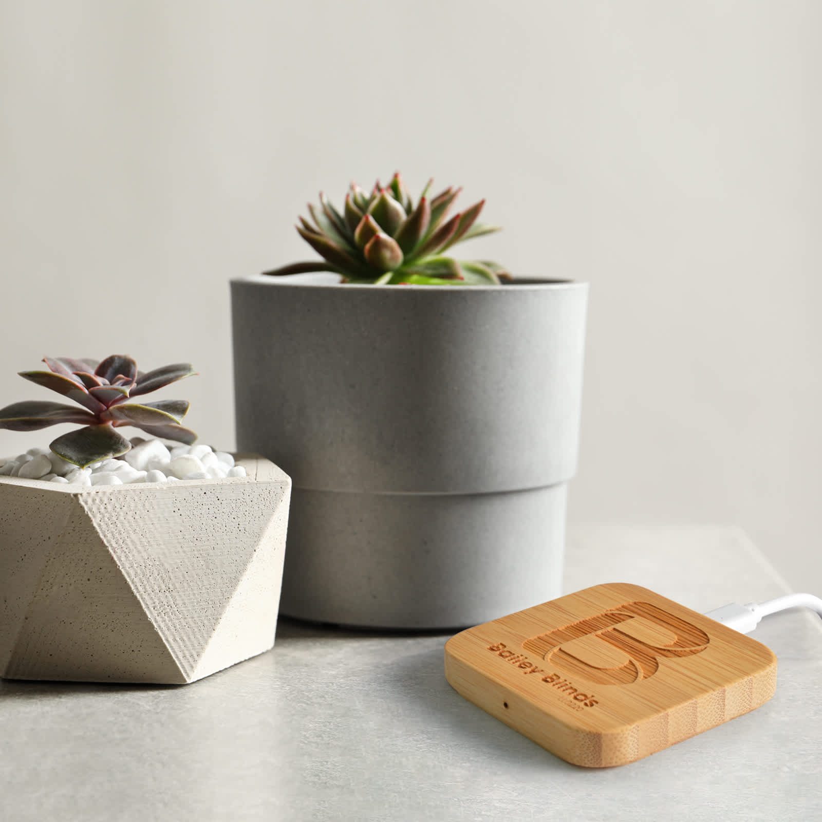 A bamboo wireless charger in a natural wood color beside two potted succulents on a light surface.