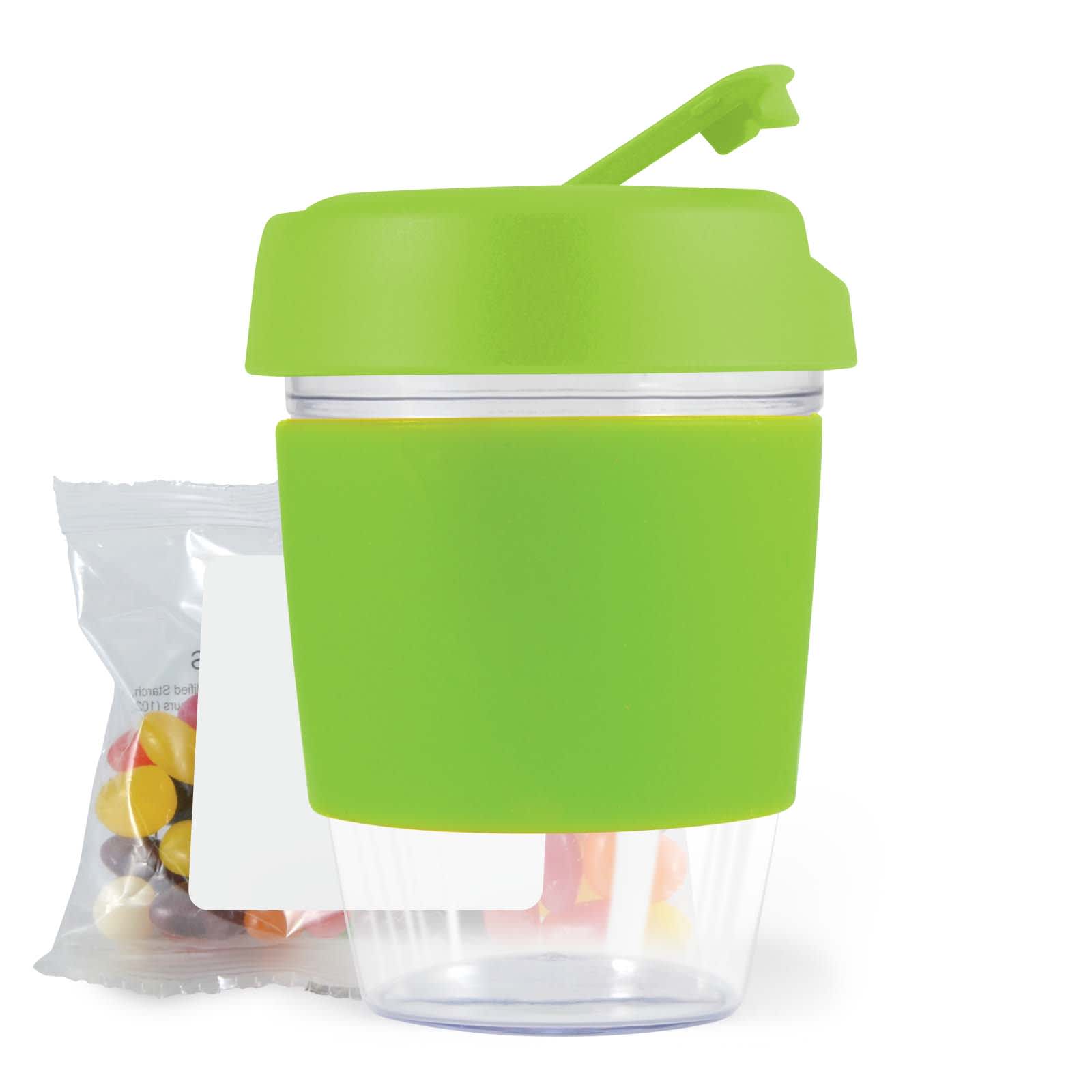 A reusable coffee cup with a bright green silicone sleeve and lid, accompanied by a small bag of colorful jelly beans.
