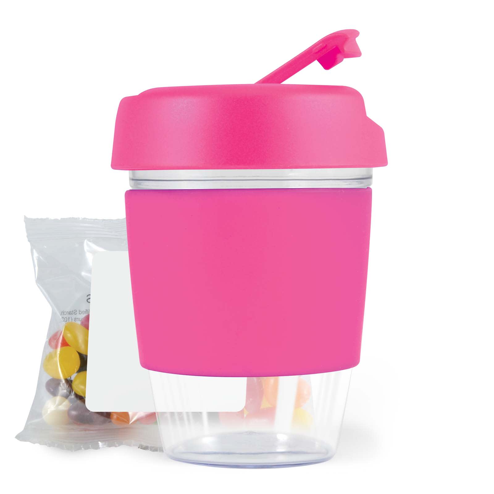 A pink reusable coffee cup with a clear base and a lid, accompanied by a bag of colorful jelly beans.