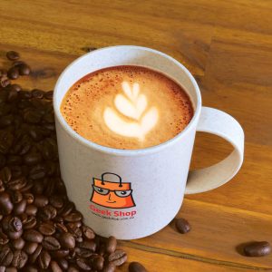 A reusable coffee mug in light beige with a logo, filled with coffee and surrounded by coffee beans.