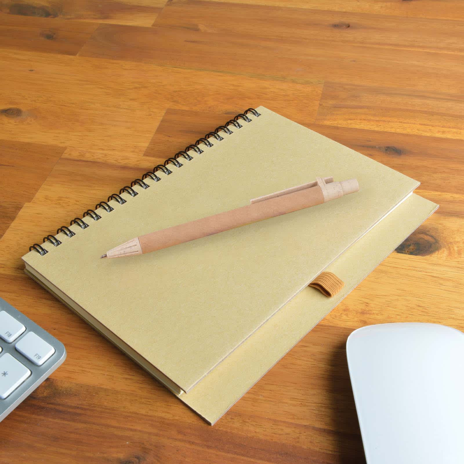 A Savannah Notebook with a spiral binding sits on a wooden surface next to an Eco Matador Pen.