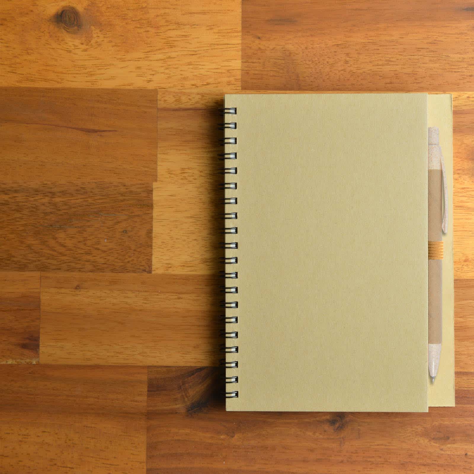 A beige spiral-bound notebook sits on a wooden surface, accompanied by a matching eco-friendly pen.
