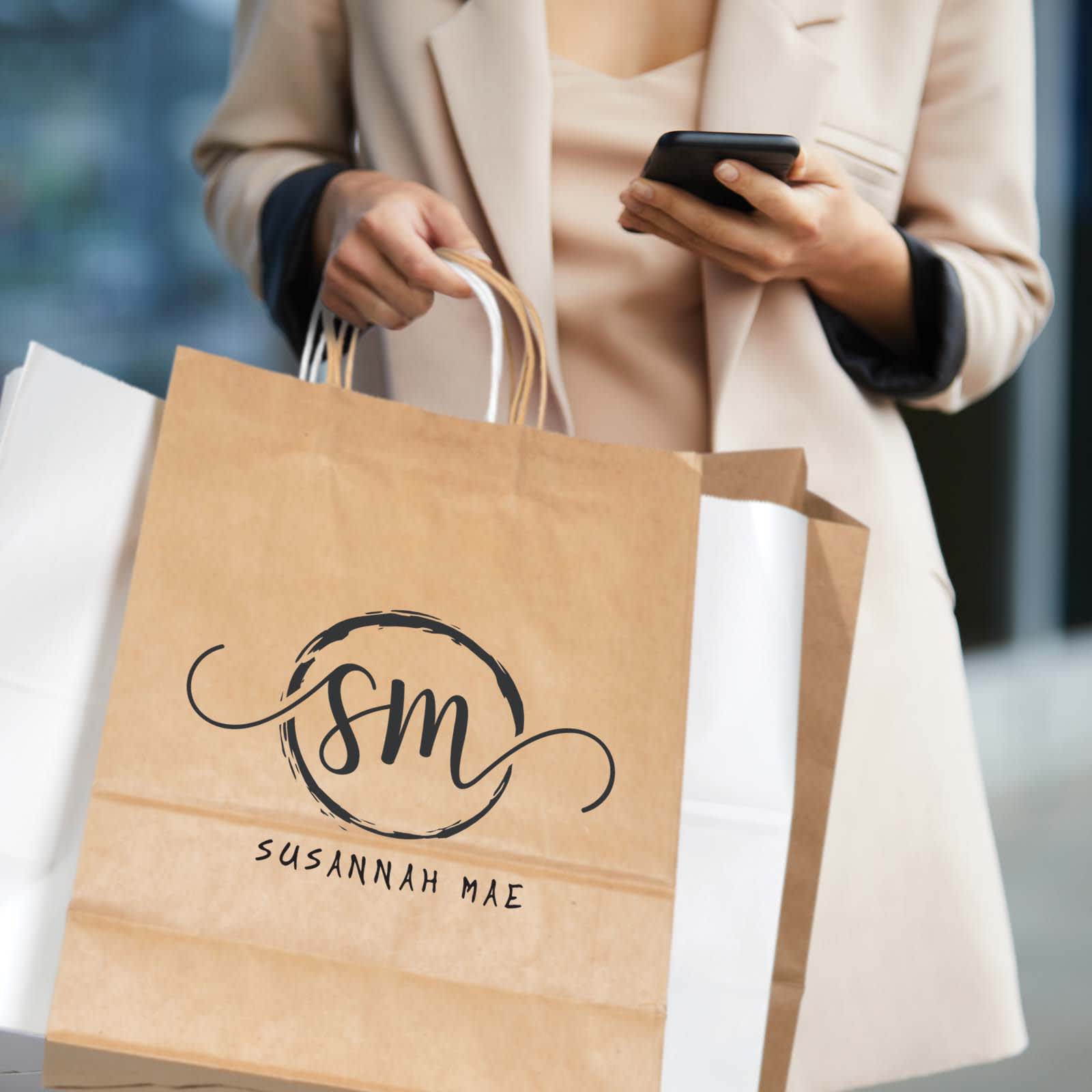 A medium-sized brown paper bag with handles and a logo, held by a person using a smartphone.