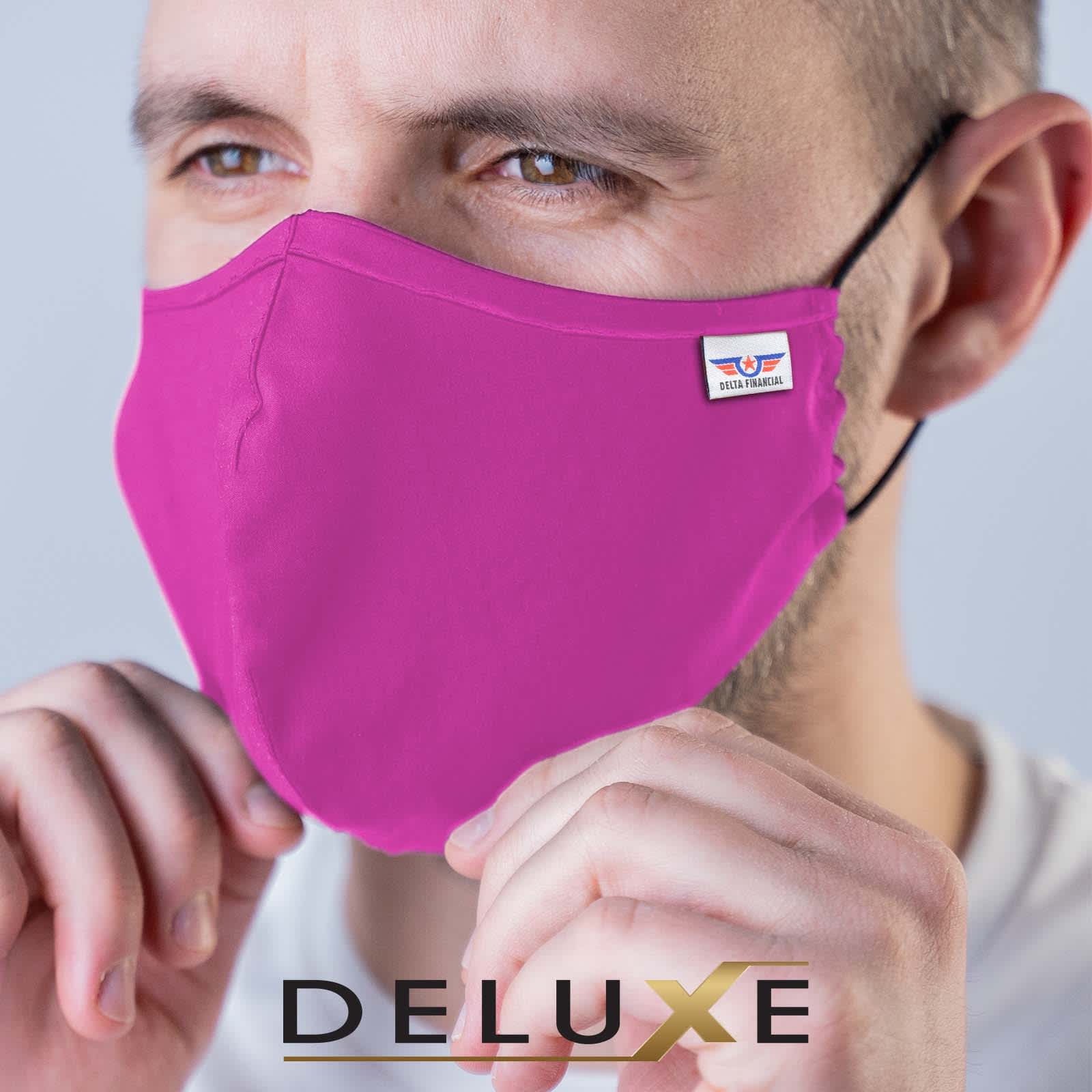 A pink deluxe adult face mask is being held by a person, featuring a logo on the side.