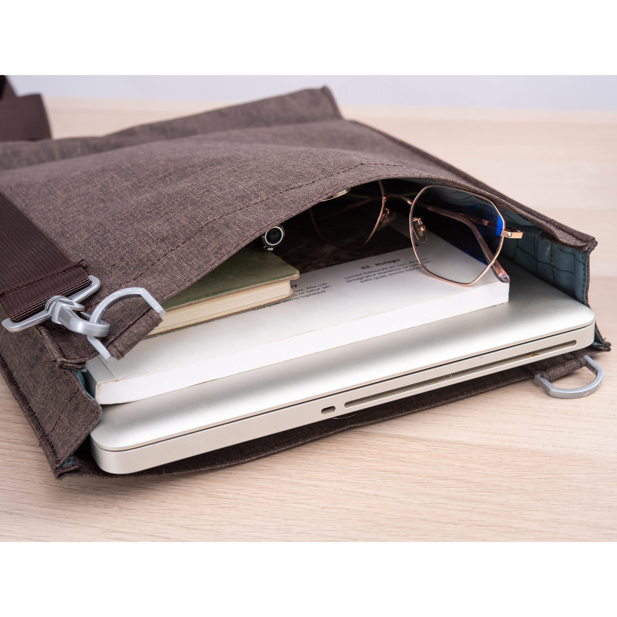 A brown nylon library bag with a laptop, notebook, and glasses peeking out from the open top. It has a logo.