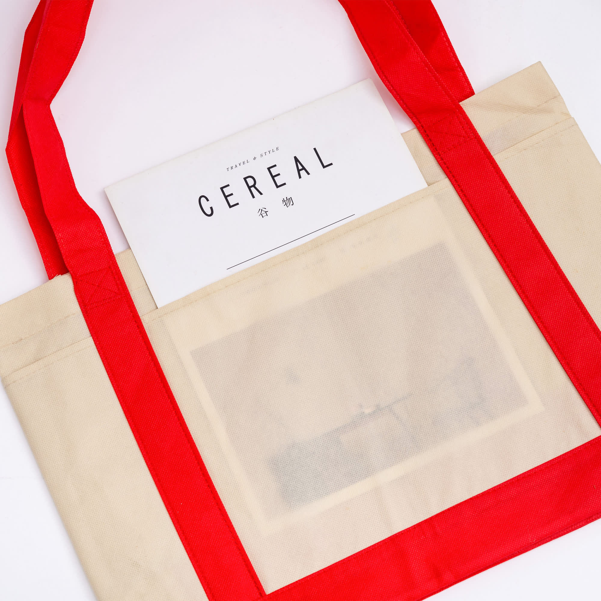A beige reusable grocery bag with red handles and a logo, holding a magazine titled 
