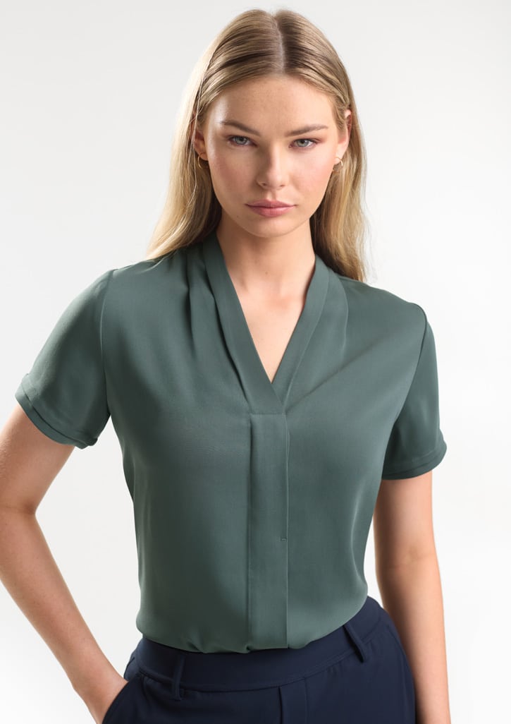 Female model wearing a seafoam green short sleeve corporate blouse with a soft V-neck collar and concealed front placket. The lightweight business top offers a contemporary, professional look suitable for corporate uniforms, office teams, hospitality staff and customer-facing workplace environments.