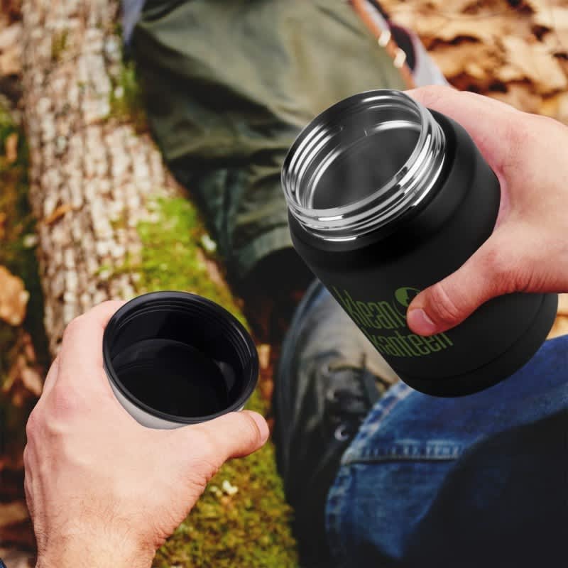 A drink bottle with a black exterior and a silver rim, held in hands against a natural background.